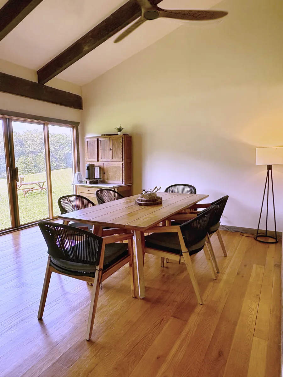 A long table and chairs in the barn apartment, with sliding doors onto the field beyond