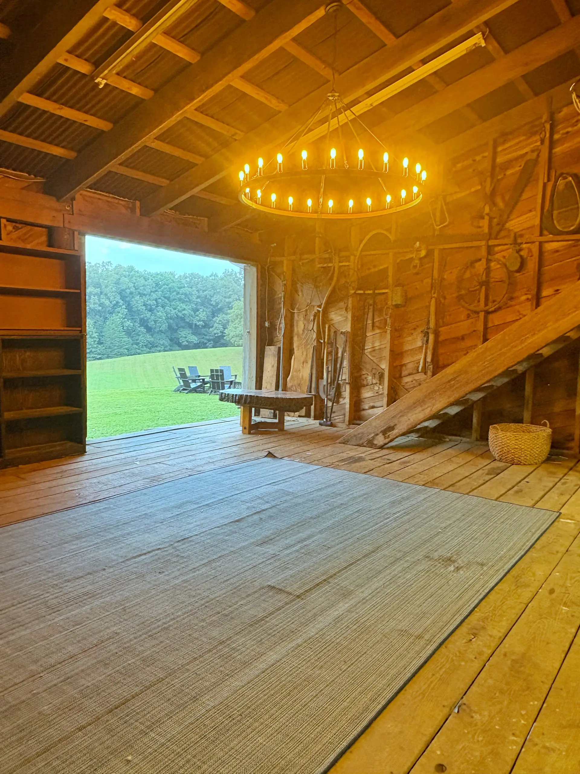 The barn's open shop half, its sliding door raised onto the field, with a chandelier above the plank floor
