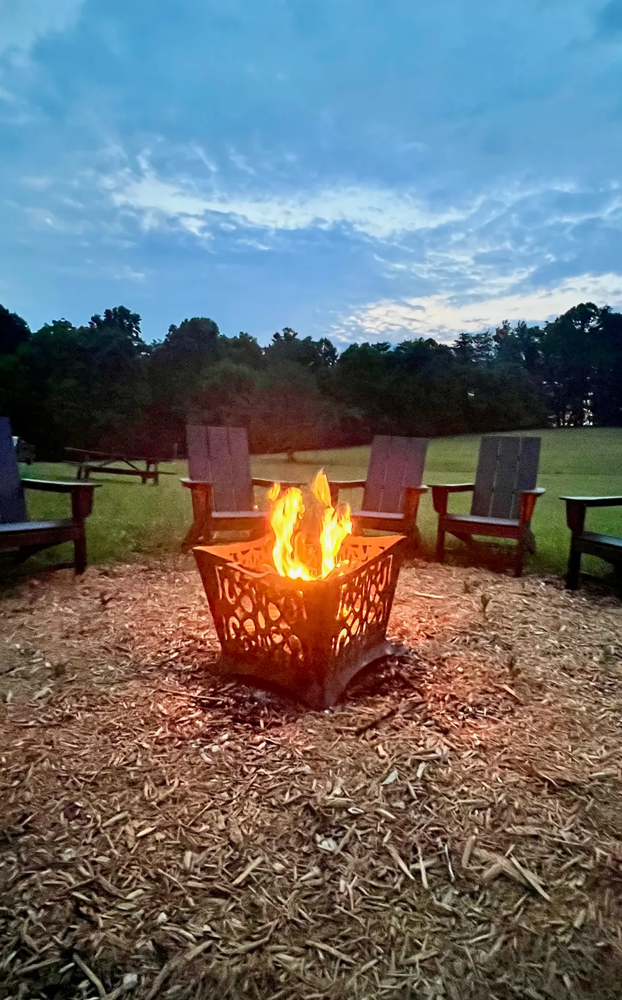 A fire burning in the fire pit, chairs drawn around it, the last blue light in the sky behind