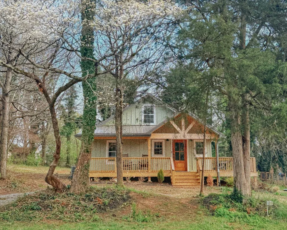 Lucky Find Cottage: a green cottage with a covered wooden porch, set among trees in spring